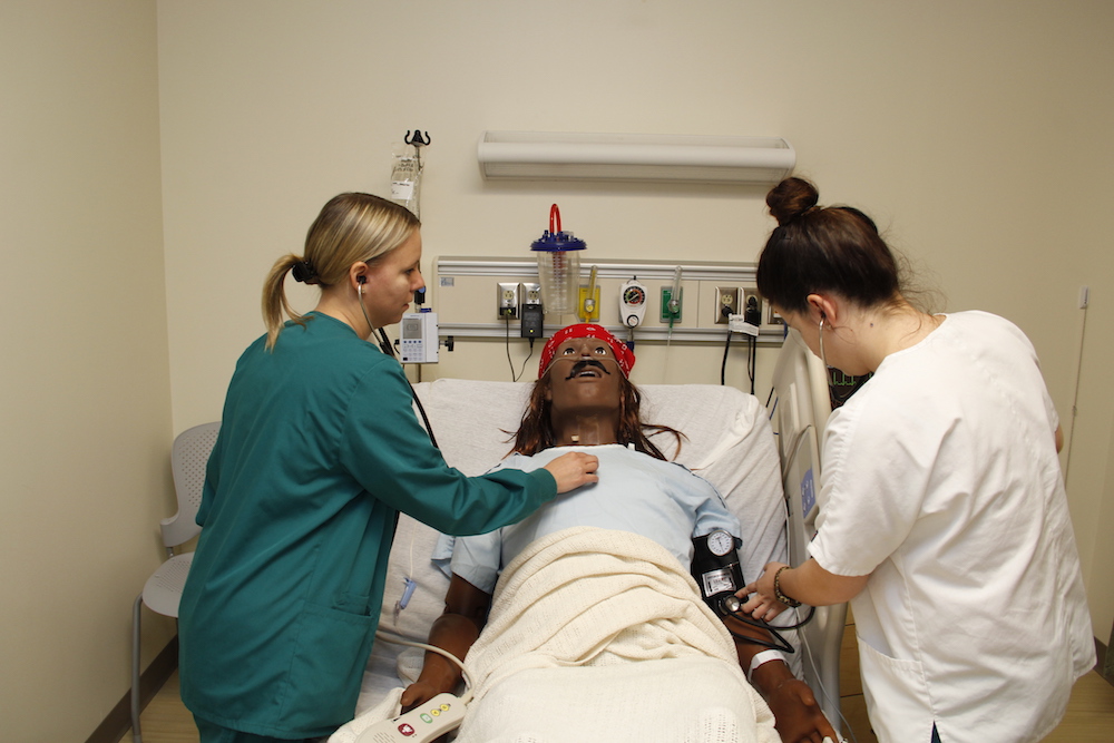 Two healthcare students practice on a patient simulator